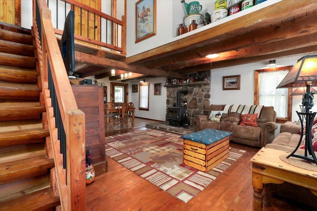 living area with beam ceiling, a wood stove, stairs, and hardwood / wood-style floors