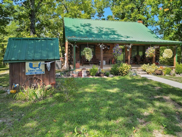 view of front of home with a chimney, a porch, a front yard, metal roof, and log exterior