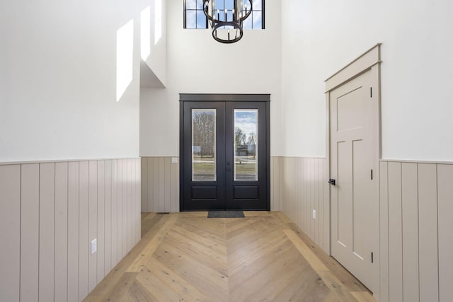 entryway featuring a wainscoted wall, french doors, wood finished floors, and a chandelier