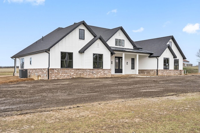 modern farmhouse style home featuring roof with shingles, brick siding, board and batten siding, and cooling unit