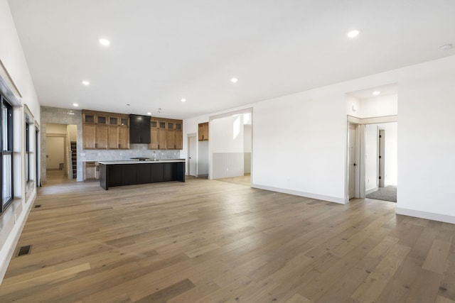 kitchen with light wood finished floors, tasteful backsplash, recessed lighting, light countertops, and open floor plan