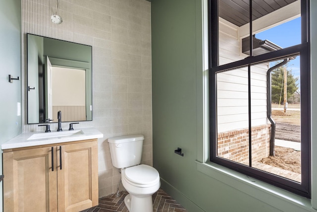 bathroom with brick floor, toilet, vanity, baseboards, and tile walls