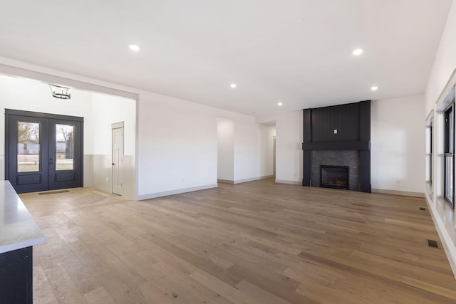 unfurnished living room with light wood-type flooring, a large fireplace, recessed lighting, and french doors