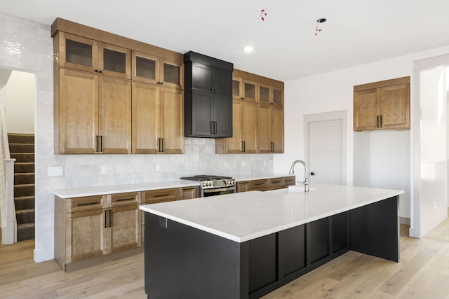 kitchen featuring a sink, light wood-style floors, stainless steel gas range, backsplash, and a large island with sink