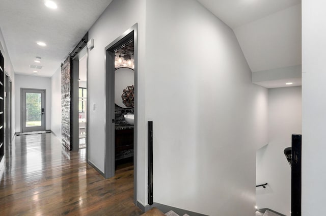 hallway featuring a barn door, dark wood-type flooring, lofted ceiling, and a textured ceiling