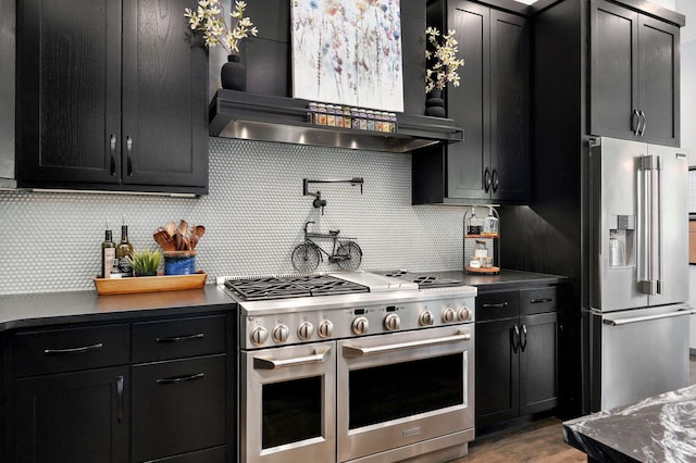 kitchen with tasteful backsplash, wall chimney range hood, dark wood-type flooring, and premium appliances