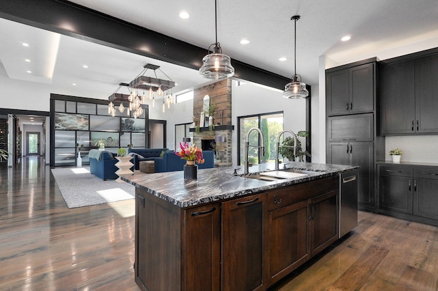 kitchen with pendant lighting, stainless steel dishwasher, a center island with sink, dark hardwood / wood-style floors, and dark stone counters