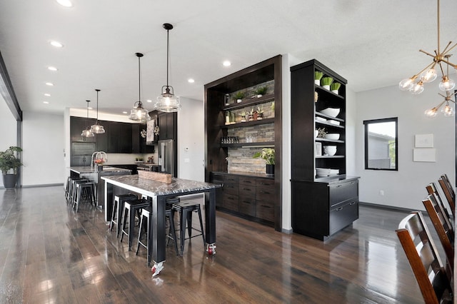 kitchen with an island with sink, a breakfast bar area, dark wood-type flooring, and stainless steel refrigerator