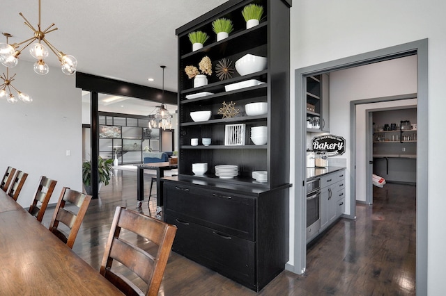 bar with an inviting chandelier, oven, dark hardwood / wood-style floors, hanging light fixtures, and a textured ceiling