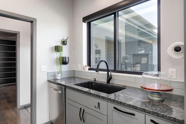 kitchen featuring stainless steel dishwasher, sink, dark hardwood / wood-style flooring, dark stone counters, and white cabinetry