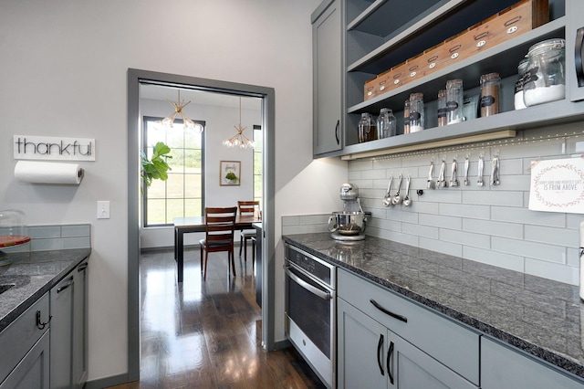 bar featuring backsplash, dark wood-type flooring, gray cabinets, stainless steel oven, and a notable chandelier