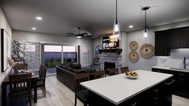 kitchen with a center island, a sink, light countertops, a fireplace, and dark cabinets