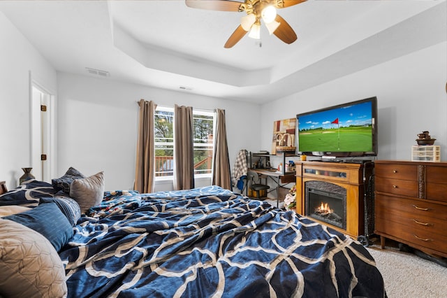 bedroom with a raised ceiling, carpet, and ceiling fan