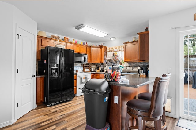 kitchen featuring black appliances, decorative backsplash, light hardwood / wood-style floors, kitchen peninsula, and a kitchen breakfast bar