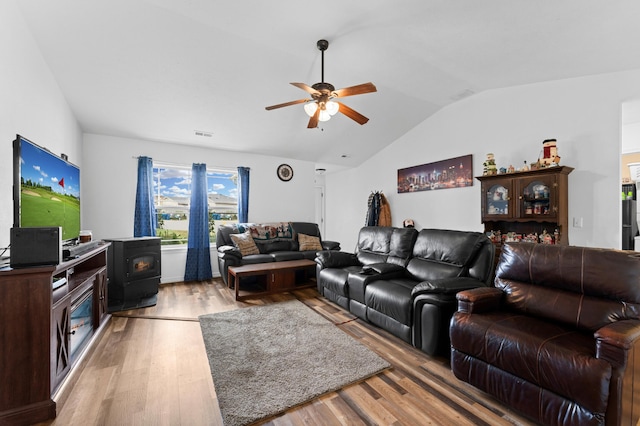 living room with ceiling fan, vaulted ceiling, light hardwood / wood-style flooring, and a wood stove