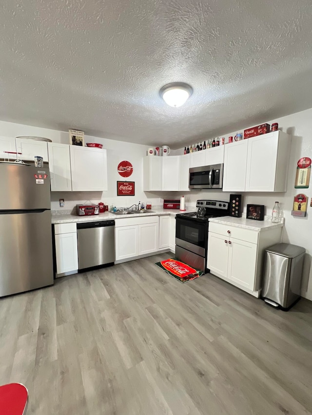 kitchen with white cabinetry, a textured ceiling, light hardwood / wood-style floors, and stainless steel appliances