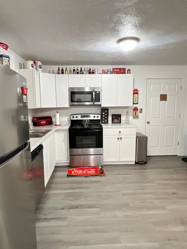 kitchen featuring white cabinetry, light wood-type flooring, appliances with stainless steel finishes, and a textured ceiling