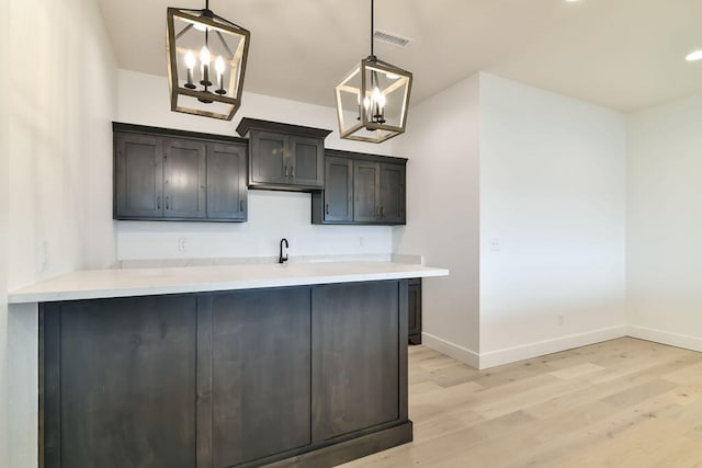 kitchen with sink, kitchen peninsula, a notable chandelier, hanging light fixtures, and light hardwood / wood-style flooring