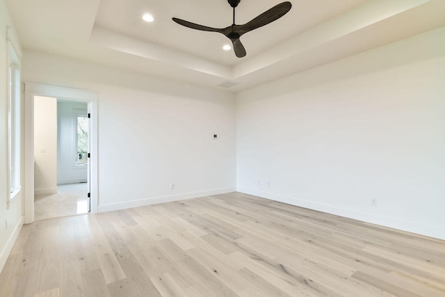 empty room with ceiling fan, a raised ceiling, and light hardwood / wood-style floors