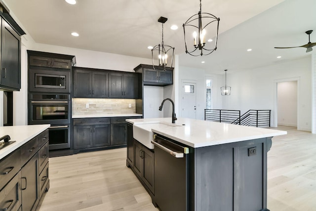 kitchen featuring light hardwood / wood-style floors, sink, stainless steel appliances, hanging light fixtures, and an island with sink