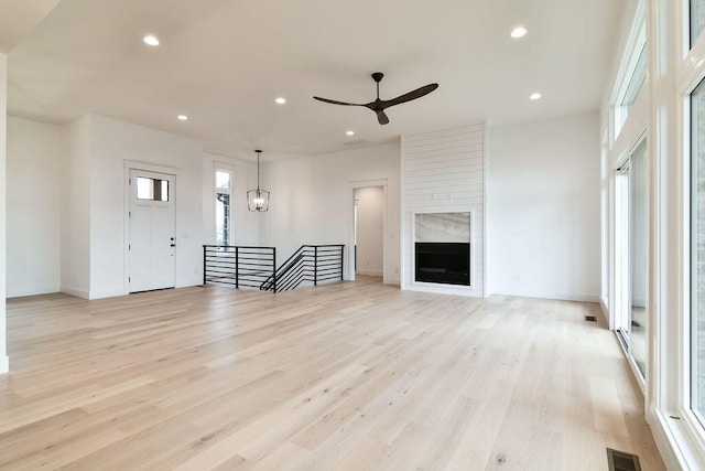 unfurnished living room featuring a large fireplace, light hardwood / wood-style flooring, and ceiling fan