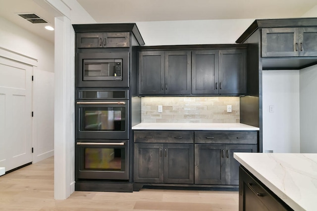 kitchen with light wood-type flooring, light stone countertops, stainless steel appliances, and tasteful backsplash