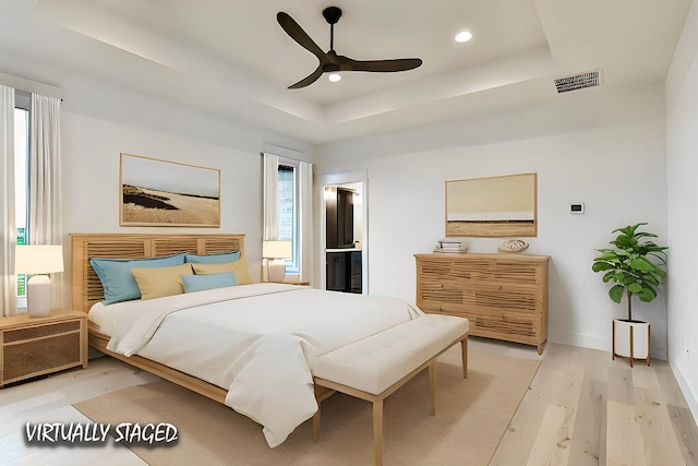 bedroom with ceiling fan, light wood-type flooring, a raised ceiling, and multiple windows