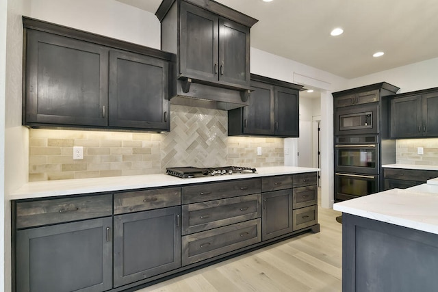 kitchen with appliances with stainless steel finishes, light stone counters, backsplash, and light hardwood / wood-style flooring