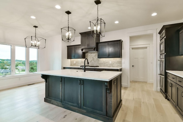 kitchen with a center island with sink, hanging light fixtures, tasteful backsplash, and light hardwood / wood-style flooring