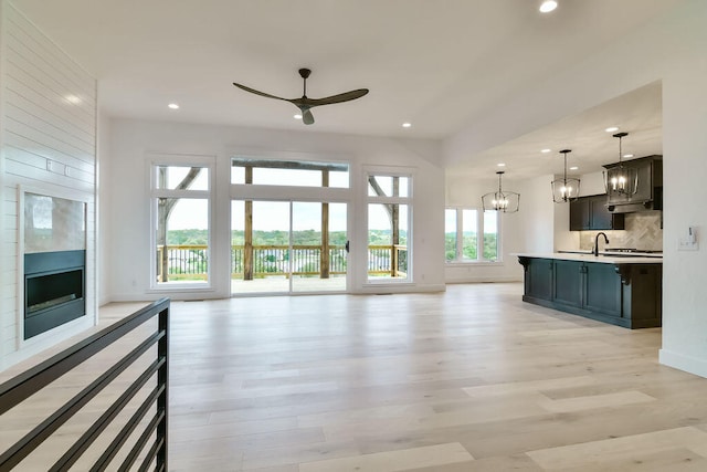 unfurnished living room featuring sink, ceiling fan with notable chandelier, light hardwood / wood-style floors, and a large fireplace