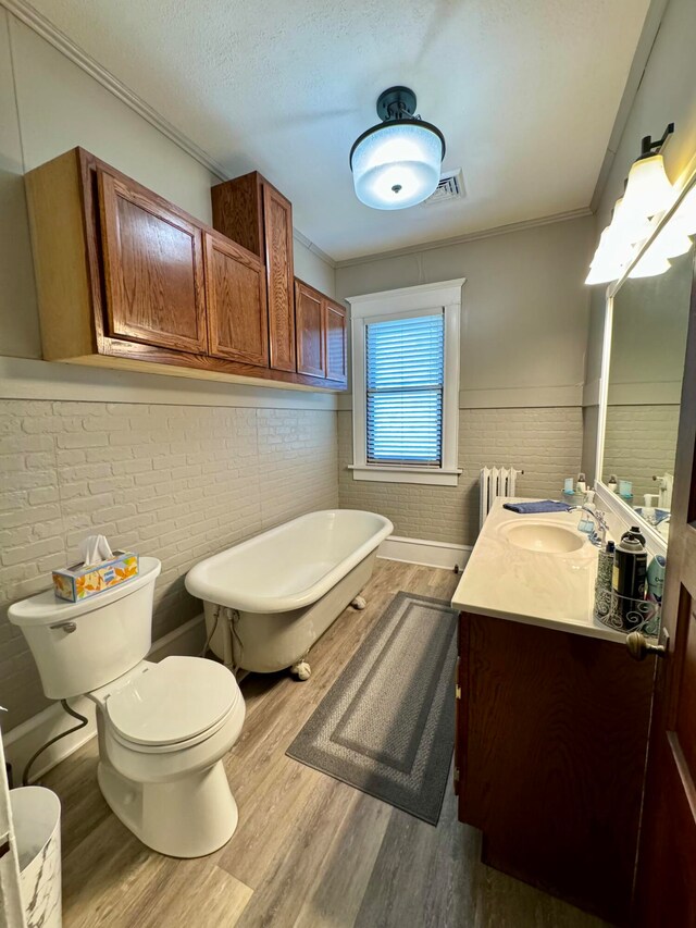 bathroom featuring radiator, brick wall, a tub to relax in, wood-type flooring, and vanity