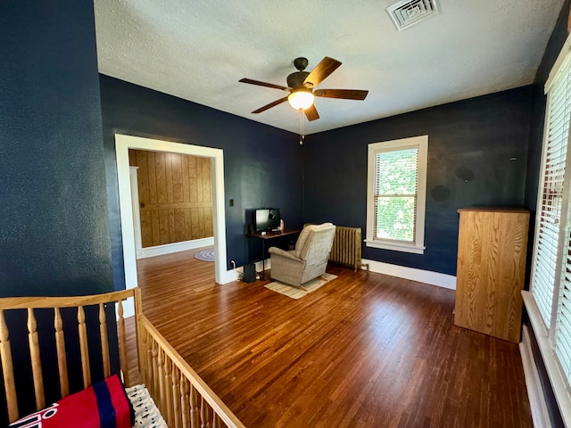 living area with ceiling fan, dark hardwood / wood-style flooring, and a textured ceiling