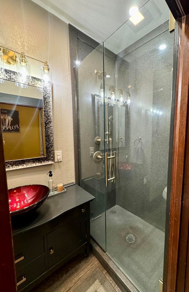 bathroom with a shower with shower door, wood-type flooring, a textured ceiling, and vanity