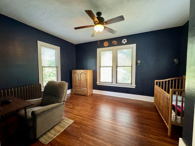 bedroom with hardwood / wood-style floors, ceiling fan, a crib, and a textured ceiling