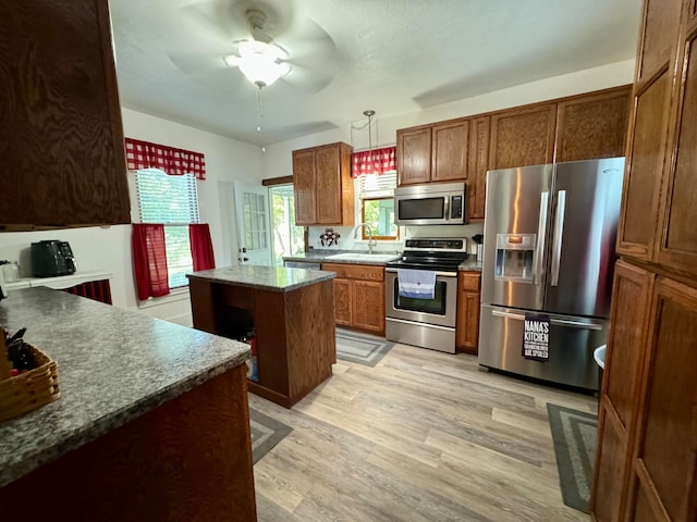 kitchen with stainless steel appliances, sink, decorative light fixtures, light hardwood / wood-style floors, and a kitchen island