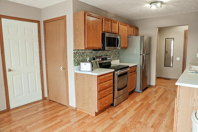 kitchen with appliances with stainless steel finishes, light wood-type flooring, decorative backsplash, and a textured ceiling