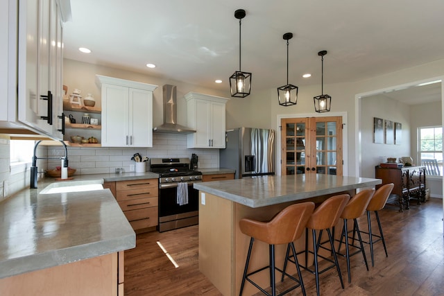 kitchen featuring wall chimney range hood, dark hardwood / wood-style flooring, stainless steel appliances, a center island, and white cabinetry