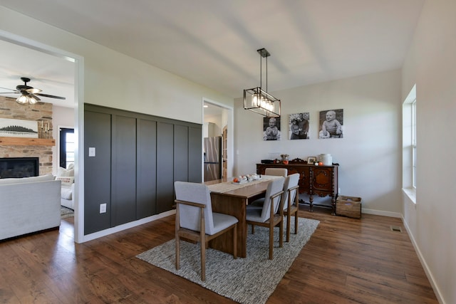 dining space featuring ceiling fan, a stone fireplace, and dark hardwood / wood-style floors