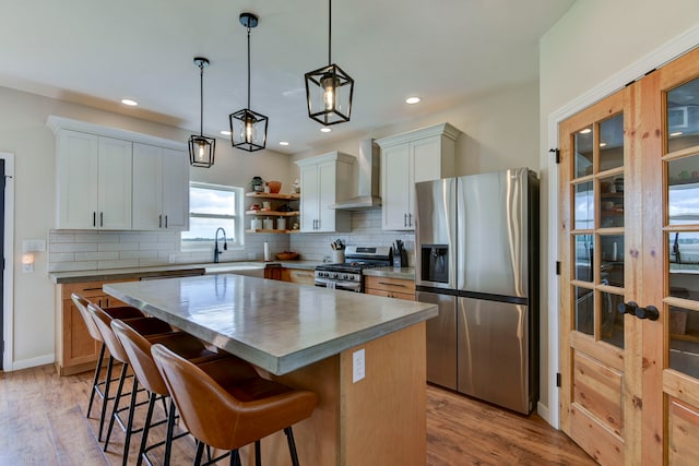 kitchen with wall chimney range hood, light wood-type flooring, appliances with stainless steel finishes, a center island, and white cabinetry