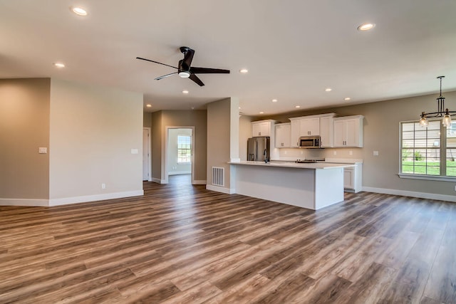 kitchen featuring wood-type flooring, ceiling fan with notable chandelier, stainless steel appliances, and white cabinets