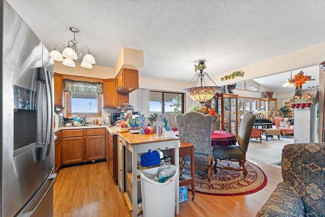 kitchen with pendant lighting, stainless steel refrigerator with ice dispenser, ceiling fan with notable chandelier, and light hardwood / wood-style floors