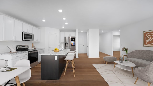 kitchen with white cabinets, recessed lighting, stainless steel appliances, wood finished floors, and a kitchen bar