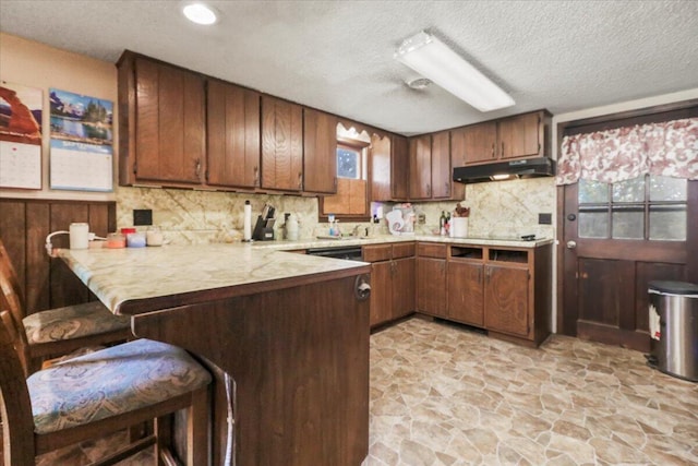 kitchen with tasteful backsplash, kitchen peninsula, a kitchen bar, and a textured ceiling