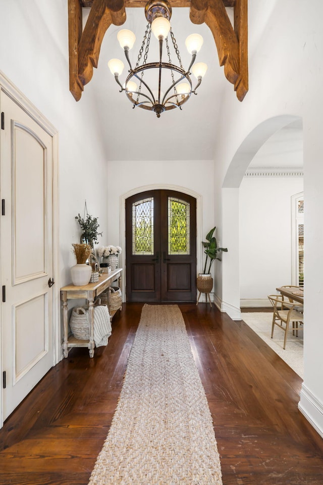 entryway featuring vaulted ceiling, arched walkways, a chandelier, and dark wood finished floors