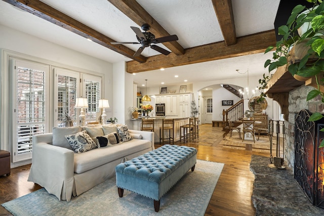 living area with wood finished floors, arched walkways, beam ceiling, stairs, and ceiling fan