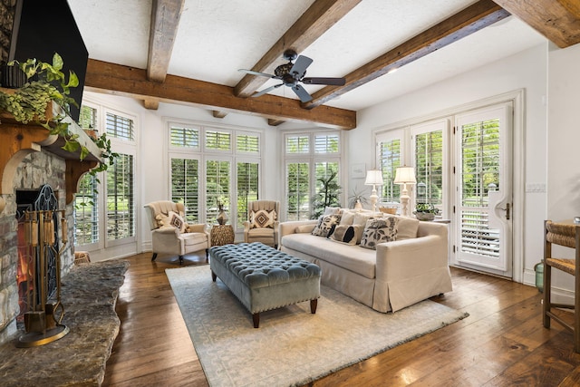 living room featuring beamed ceiling, plenty of natural light, dark wood-type flooring, and a stone fireplace