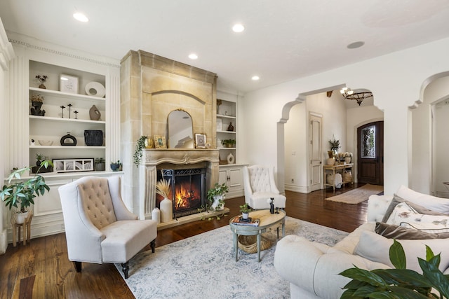 living room featuring recessed lighting, dark wood-style floors, arched walkways, built in features, and a large fireplace