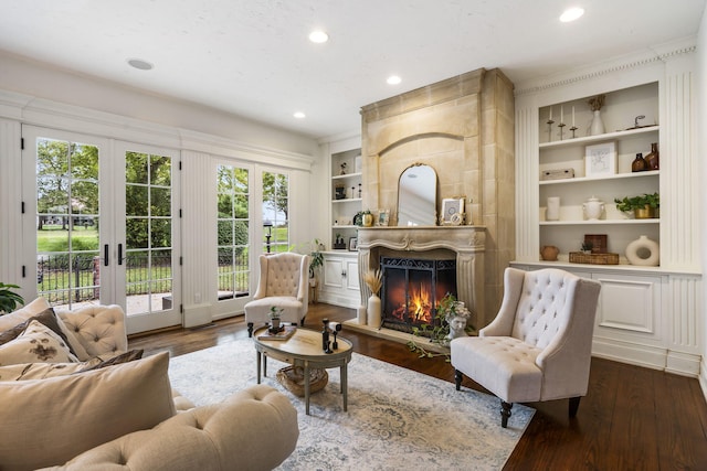 sitting room with a large fireplace, built in features, dark hardwood / wood-style floors, and french doors