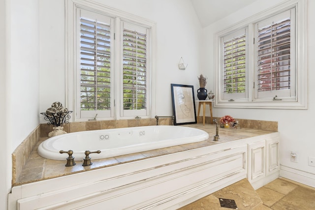 bathroom with a bath, a wealth of natural light, stone finish floor, and vaulted ceiling