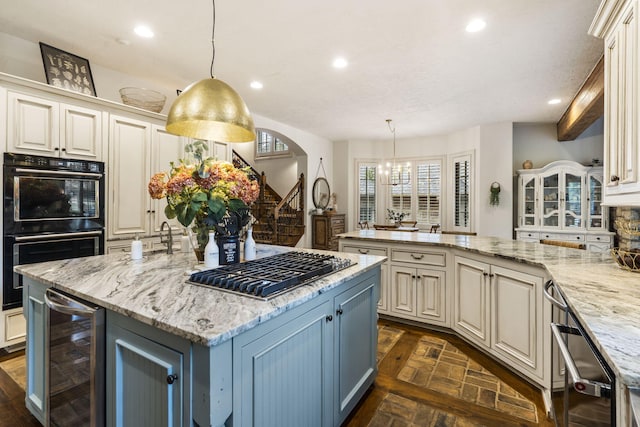 kitchen with light stone counters, black double oven, hanging light fixtures, a spacious island, and wine cooler